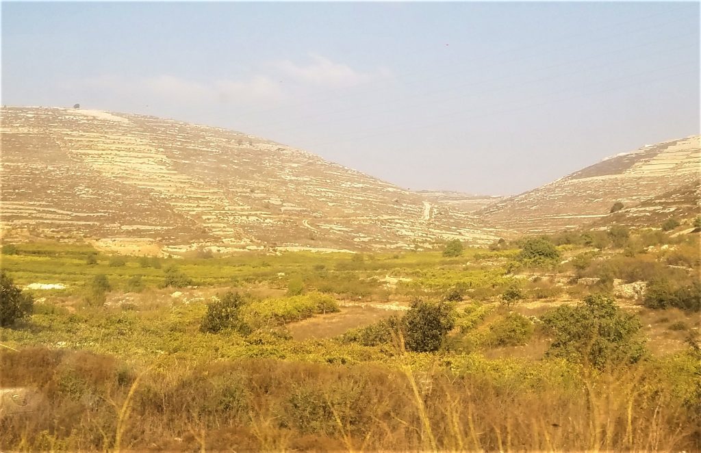 Green agricultural valleys overseen by barren rocky hills.