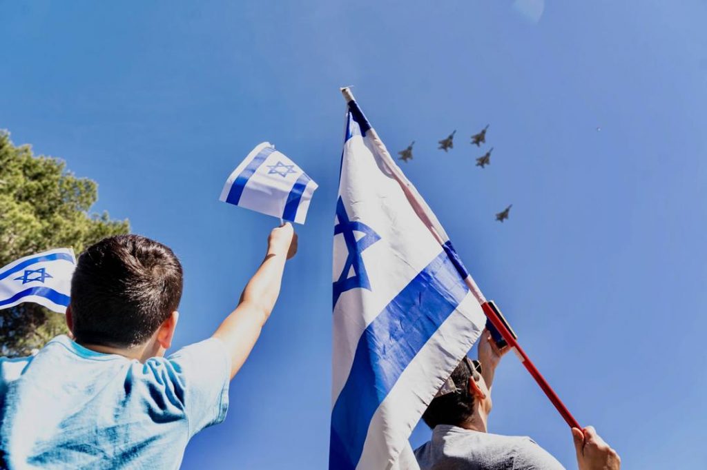 Flag waving father and son watching F16s overhead.